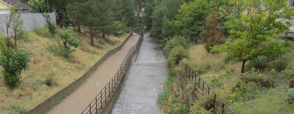 Photo of water flowing in a step-wise channelized stream. A paved pedestrian path follows the side of the stream.