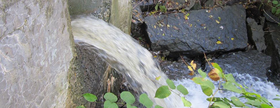 Photo of stormwater discharging from a concrete drainage structure into a rock-lined drainage pathway.
